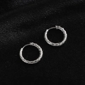 Macro shot of silver hoop earrings featuring a textured quilted pattern on black silk - Quilted Pattern / Steel