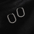Detailed view of silver beaded hoop earrings on black silk texture background - Oval Beaded / Steel