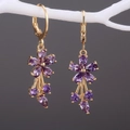 Detail von goldenen Blumenohrringen mit lila Zirkonia, hängend an einem weißen Zweig - Lila