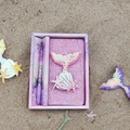 Pink mermaid stationery set with glitter notebook and ballpoint pen on beach sand - Mermaid Pink
