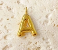 Detailed view of a 3D bubble letter A pendant in gold finish on a beige stone surface - Letter-A / Steel