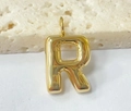 Vista macro di un ciondolo dorato lettera R con design a bolla su base in pietra - Lettera-R / Oro