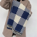 Bufanda gruesa a cuadros azul y beige con flecos, colocada sobre un abrigo de invierno - Azul
