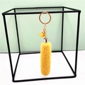 Yellow plush tassel keychain with golden metal ring hanging in a geometric black frame - Yellow