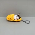 Macro detail of a plush sleeping cat keychain inside a yellow knit sleeping bag charm - Yellow