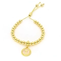 Détail d'un bracelet à billes dorées avec un pendentif lettre T en émail rose clair - Lettre T