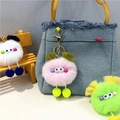 Detail of colorful plush monster keychains with tassels used as bag charms on a mini chair - Pink