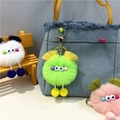 Close-up of cute plush monster charm with golden clasp on denim bag featuring tassels - Green