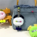 Close-up of colorful furry monster bag charms hanging on a blue denim handbag - White