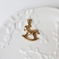 Macro shot of 18K gold rocking horse pendant on a white embossed ceramic plate - G05-Rocking Horse