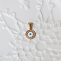 Macro view of a round 18K gold evil eye pendant with blue enamel and textured gold border - G10-Enamel Evil Eye