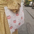 Outdoor shot of a white canvas tote bag with pink peach prints and peach lettering - Peach