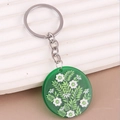 Close-up of bohemian green floral acrylic keychain with silver ring on textured surface - Green