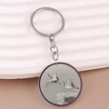 Close-up of a silver keychain with a round pendant featuring cranes and pine trees - Bird