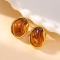 Boucles d'oreilles ovales ambre avec monture en acier titane doré sur plateau blanc - Boucles d'Oreilles Clous en Ambre Ovale