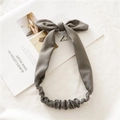 Detalle de diadema elástica gris con orejas de conejo y lazo grande sobre fondo de tela - Gris claro