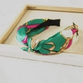 Detail eines grünen Satin-Knoten-Haarband mit goldenem Kettenmuster auf Stoff - Grün