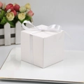 White square cardboard candy gift box with elegant white ribbon bow on a decorative tray - White
