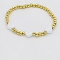 Detailed close-up of golden beaded bracelet featuring three white enamel heart charms - White
