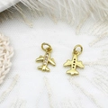 Macro detail of gold airplane pendant with crystal pavé on white lace background - Airplane