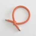 Detail of coral orange braided hair tie featuring a center knot and gold metal end caps - Orange