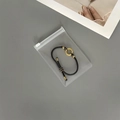 Close-up of a black cord bracelet with gold accents inside a clear EVA jewelry storage pouch - 50 Silk Transparent Zipper Bag / 9x13cm
