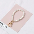 White glass pearl hand chain with golden star pendant on a pink pantone card - KC Gold Star