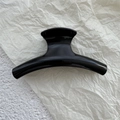 Detail of a curved glossy black hair claw clip resting on white decorative paper - Bright Black