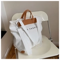 Weiße Canvas-Tasche mit braunen Lederdetails und breitem Gurt auf einem Metallstuhl - Weiß