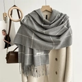 Detail eines grauen Schals mit Hahnentrittmuster, Fransen und Textiletikett - Grau