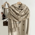 Detail of khaki houndstooth scarf with tassels draped over a beige trench coat - Apricot