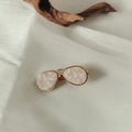 Dettaglio del fermaglio dorato con intarsio in resina bianca su tessuto bianco - Rosa