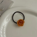Close-up of amber resin rose flower hair tie on white ceramic plate with soft lighting - Orange