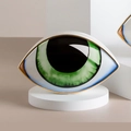 Modern ceramic Evil Eye ornament with green iris and gold rim on a white pedestal - Green