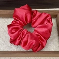 Detail of red satin oversized scrunchie showing glossy silk texture on a glass tray - Red