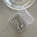 Vista macro de clips de pelo plateados retorcidos en una caja de almacenamiento clara - Horquillas Trenzadas (20 piezas) / Plateado