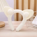 White plush cat ear headband with soft pom-poms on a wooden table for face washing - White