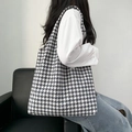Dettaglio della borsa tote in tela pied de poule su un divano in pelle nera - Houndstooth