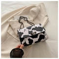Close-up of cow print crossbody bag featuring metal lock and chain strap on blazer - Cow Print