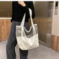 Detailed view of large white tote bag with black rivets on model in modern setting - White
