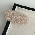 Macro shot of a soft beige plush hair clip on a neutral fabric tray detail view - Apricot