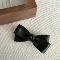 Detail of a textured black PU leather bow hair clip on a white knitted fabric background - Black