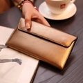 Elegante bronzefarbene Damen-Umschlaggeldbörse aus Metallic-Leder in einer Cafe-Szene - Gold