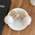 Barrette nœud en tricot beige avec pompons blancs sur une assiette blanche épurée - Kaki