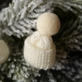 Mini bonnet de Noël tricoté blanc crème avec pompon sur une branche de sapin - Blanc Cassé