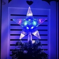 Macro shot of a transparent plastic star tree topper with blue LED light on a green branch - 15cm Striped Multicolor (2x AA Battery Box)