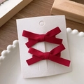 Detail view of two red ballet-style satin bow hair clips on a white card in a dish - Wine Red