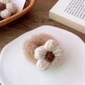 Primer plano de coletero de felpa marrón claro con una flor de punto y decorado de madera - Coletero de Peluche con Flor Beige / [atributos Del Producto] Parece Ser Una Goma Para El Pelo Minimalista De Felpa Estilo Coreano. El Cuerpo Principal Está Hecho De Un Material De Piel Sintética De Conejo De Color Marrón Claro Que Es Suave Y Esponjoso. Una Pequeña Flor Blanca Tejida A Mano Adorna El Centro.