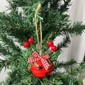 Red metal Christmas bell ornament with plaid bow and red berries hanging on a pine tree - Red Snowflake Bell