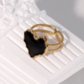 Detail eines verstellbaren Goldrings mit schwarzem Herz-Inlay auf weißem Reliefelement - Schwarz